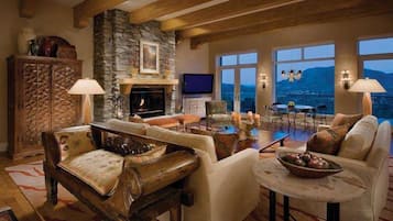 A spacious living room with a stone fireplace, comfortable seating, and large windows offering a view of the mountains.