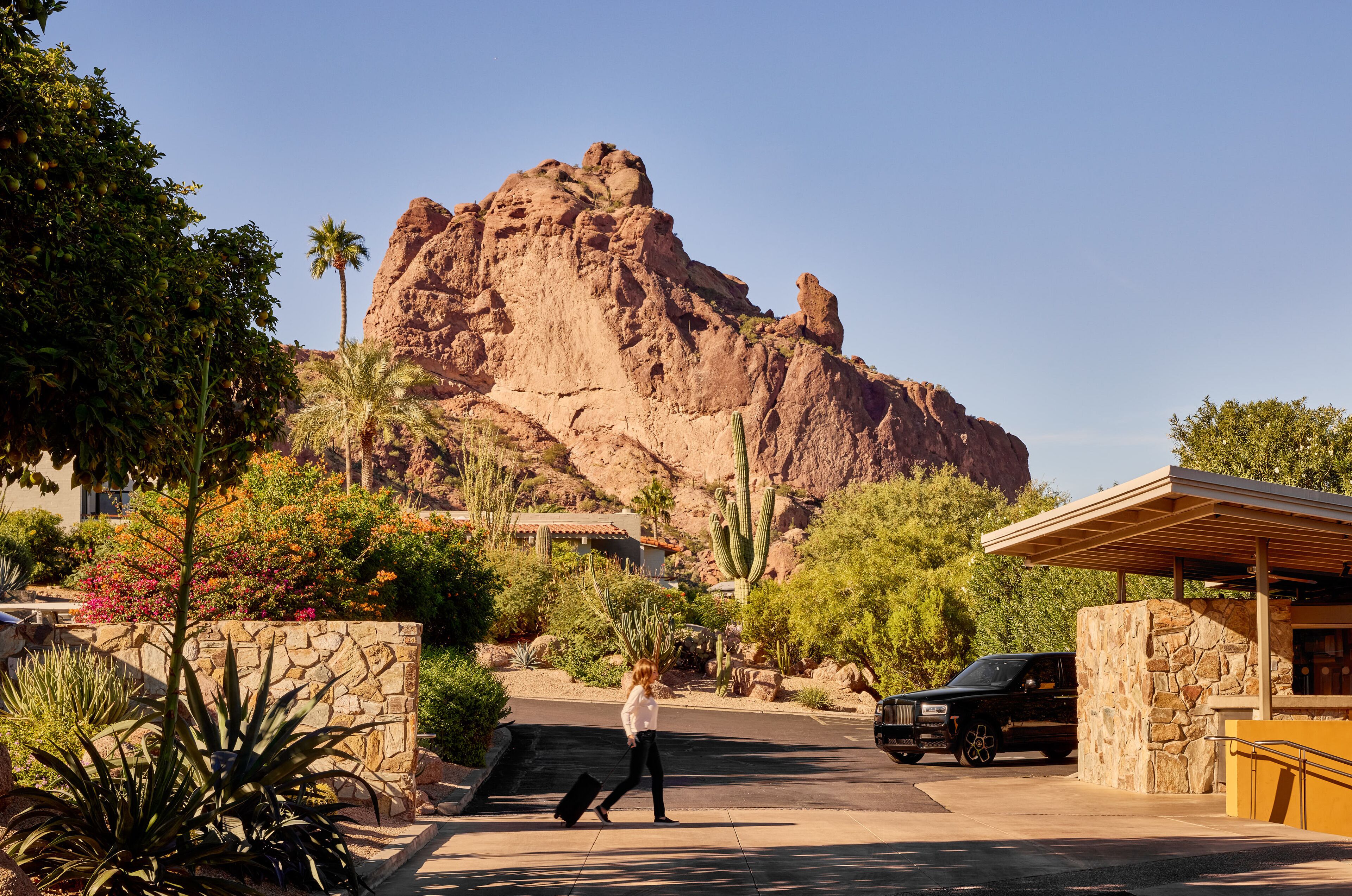 A desert landscape with a large rock formation, a paved road, and a building with a covered entrance.