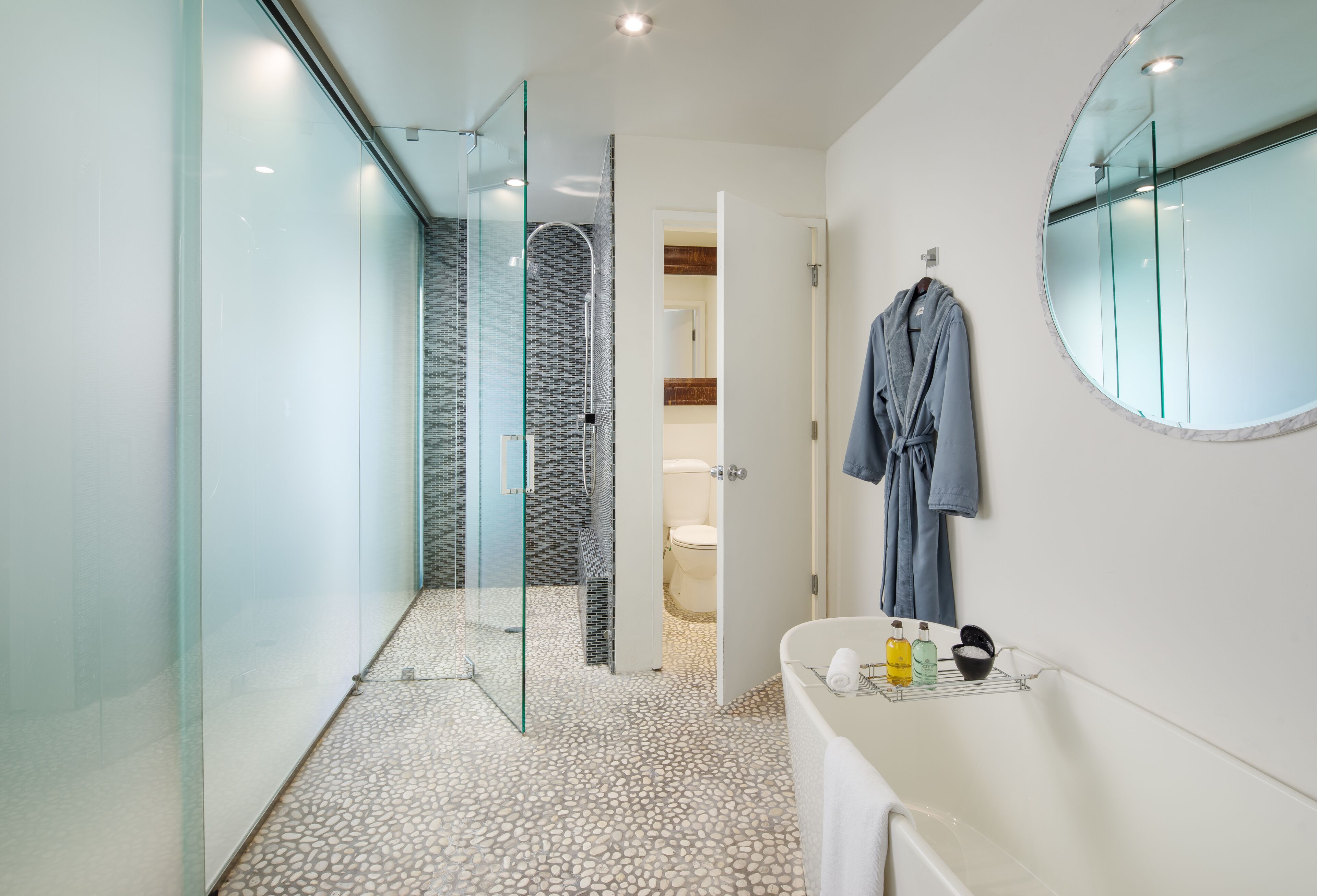 Une salle de bain moderne avec une douche à l’italienne en verre, un lavabo blanc avec un miroir et une serviette bleue accrochée au mur.
