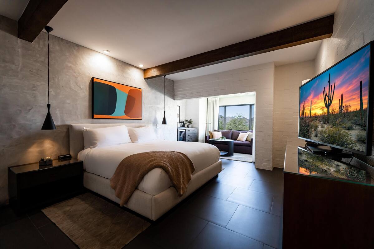 A modern bedroom with a large bed, a TV, and a painting of a desert landscape.