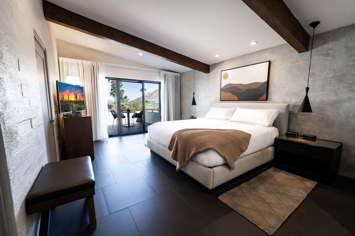 A modern bedroom with a large bed, a bench, a nightstand, and a view of the outdoors.
