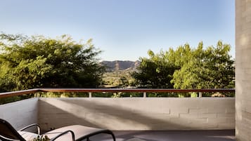 A balcony with a view of a mountainous landscape, featuring a brick wall and two chairs.