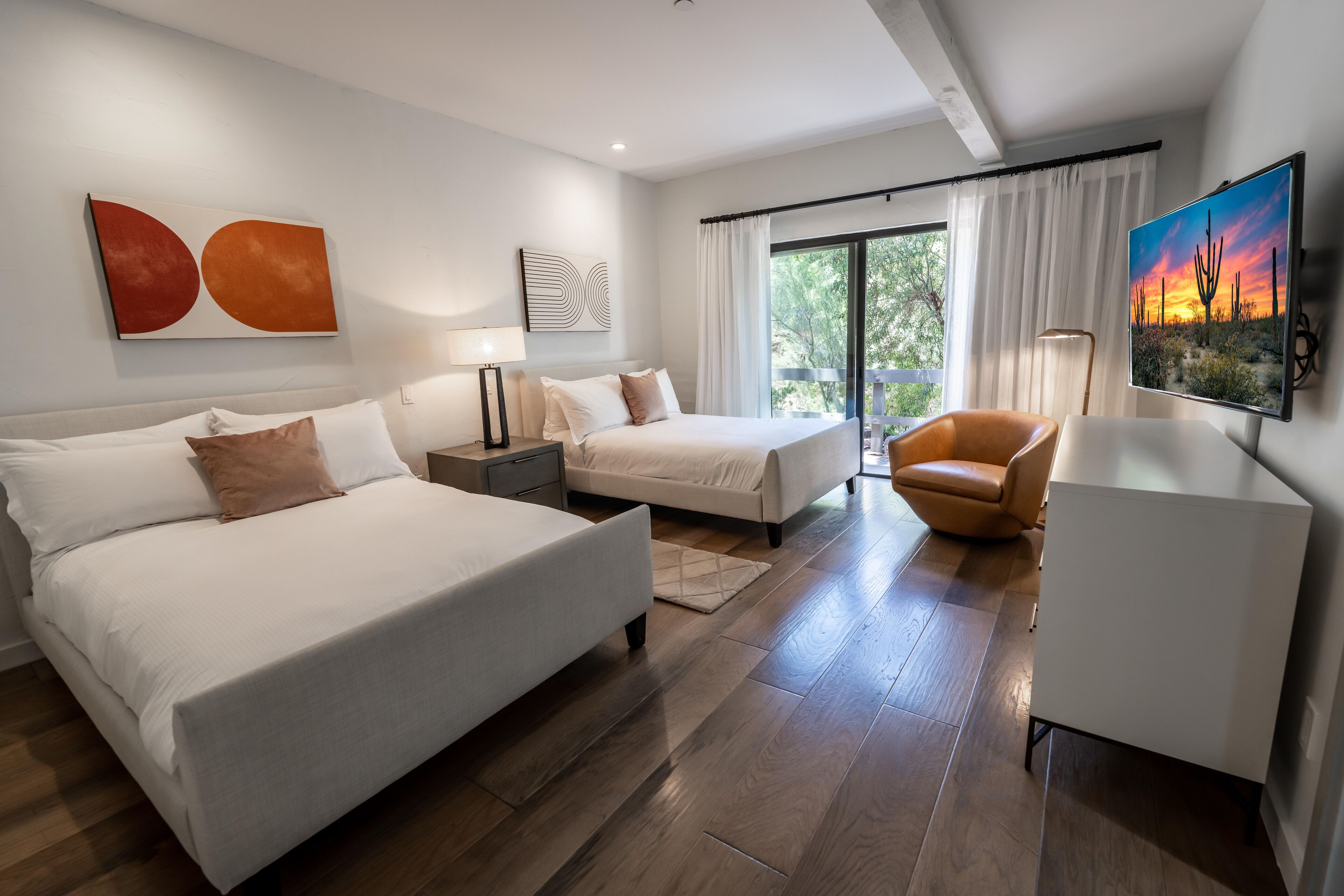 A modern hotel room with a large bed, a smaller bed, a sofa, a TV, and a balcony with curtains.