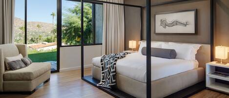 A modern bedroom with a four-poster bed, a sofa, and a large window offering a view of a landscaped garden.