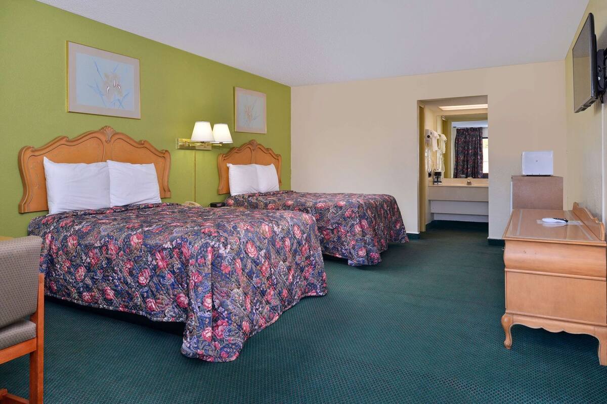 Ein Hotelzimmer mit zwei Betten, einem Schreibtisch, einem Stuhl und einem durch eine offene Tür einsehbaren Badezimmer.