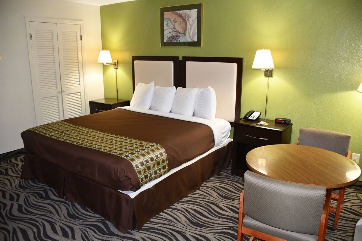 Ein Hotelzimmer mit einem Bett, Nachttischen, einem Sessel, einem kleinen Tisch und einem an der Wand montierten Telefon.