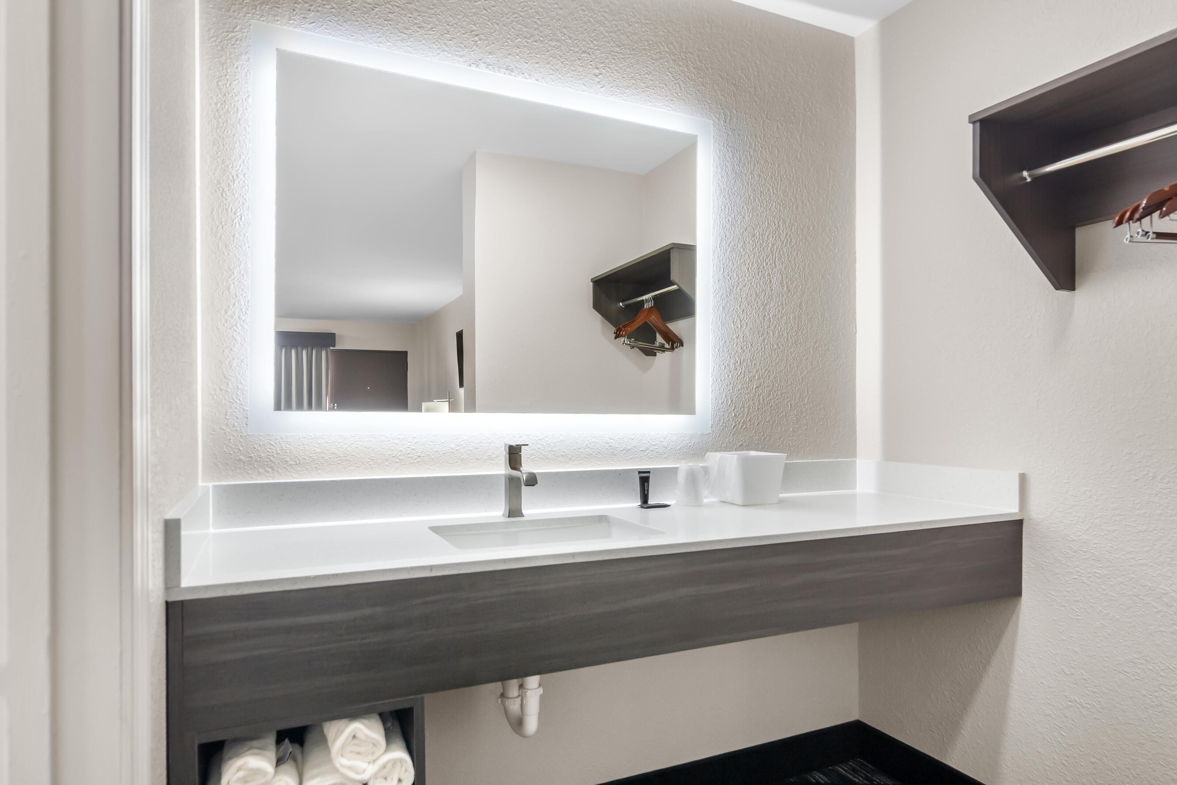 A modern bathroom with a large mirror, a white sink, and a dark countertop.