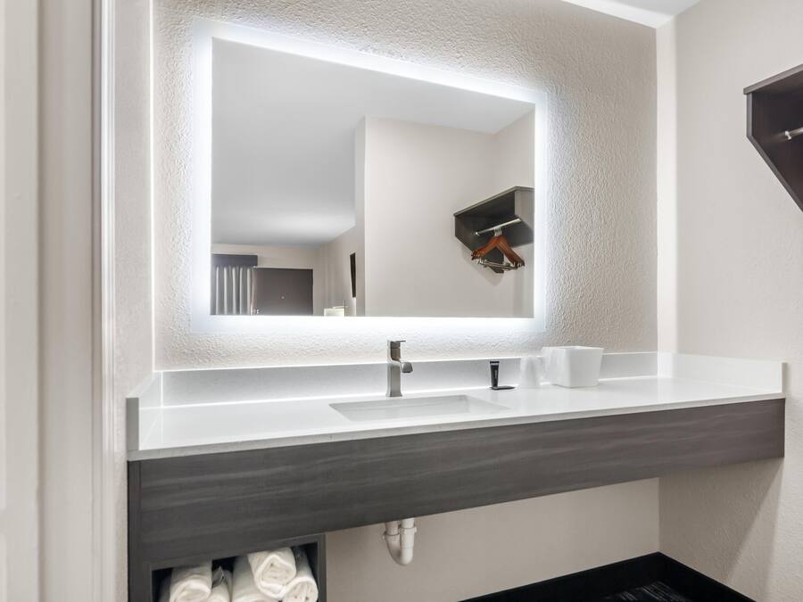 A modern bathroom with a large mirror, a white sink, and a dark countertop.