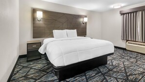 A hotel room with a bed, bedside tables, a headboard with wall sconces, a window with curtains, and a patterned carpet. - Americas Best Value Inn Bishopville (Bishopville)