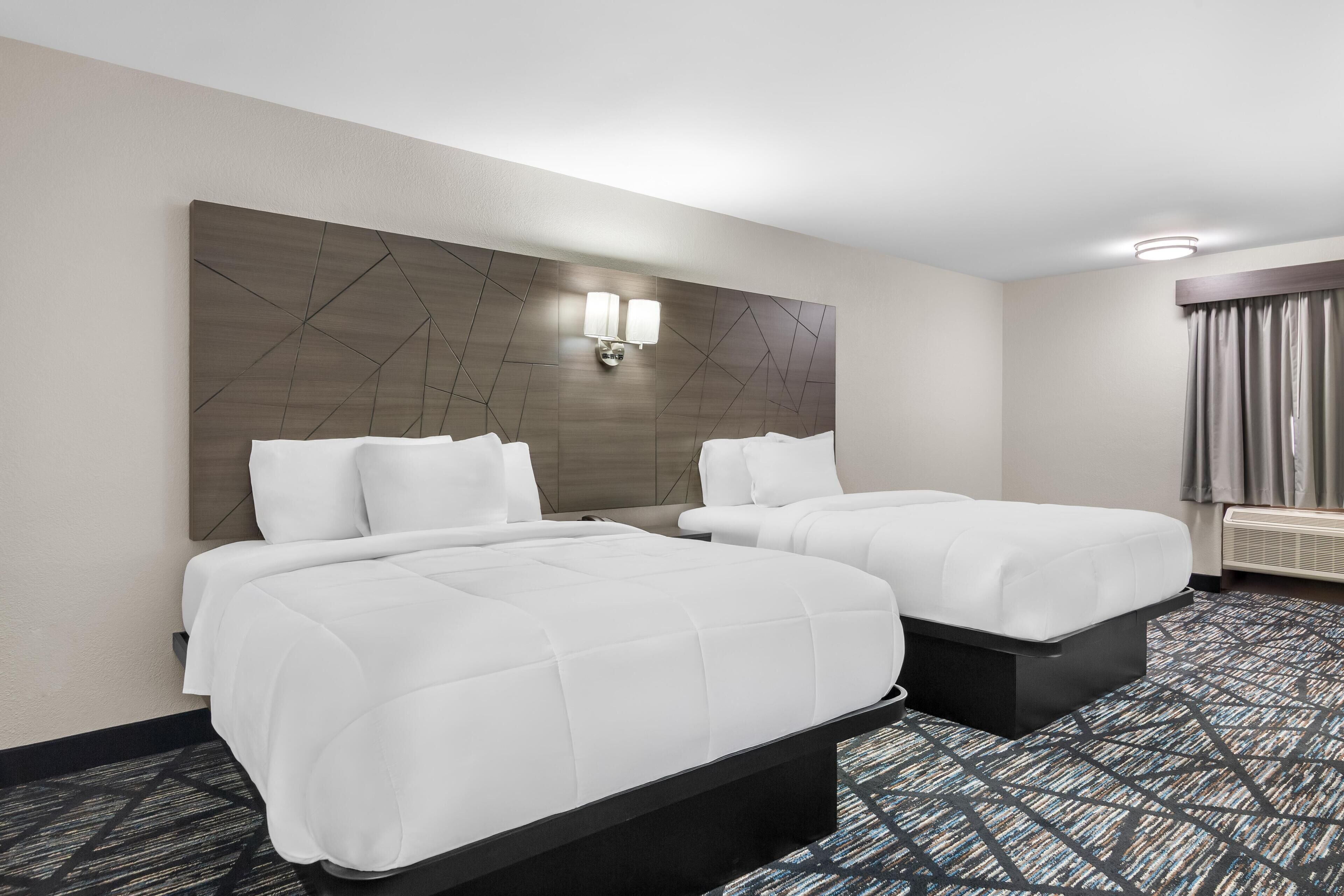 Ett hotellrum med två sängar, en stor väggmonterad lampa och en mönstrad matta.