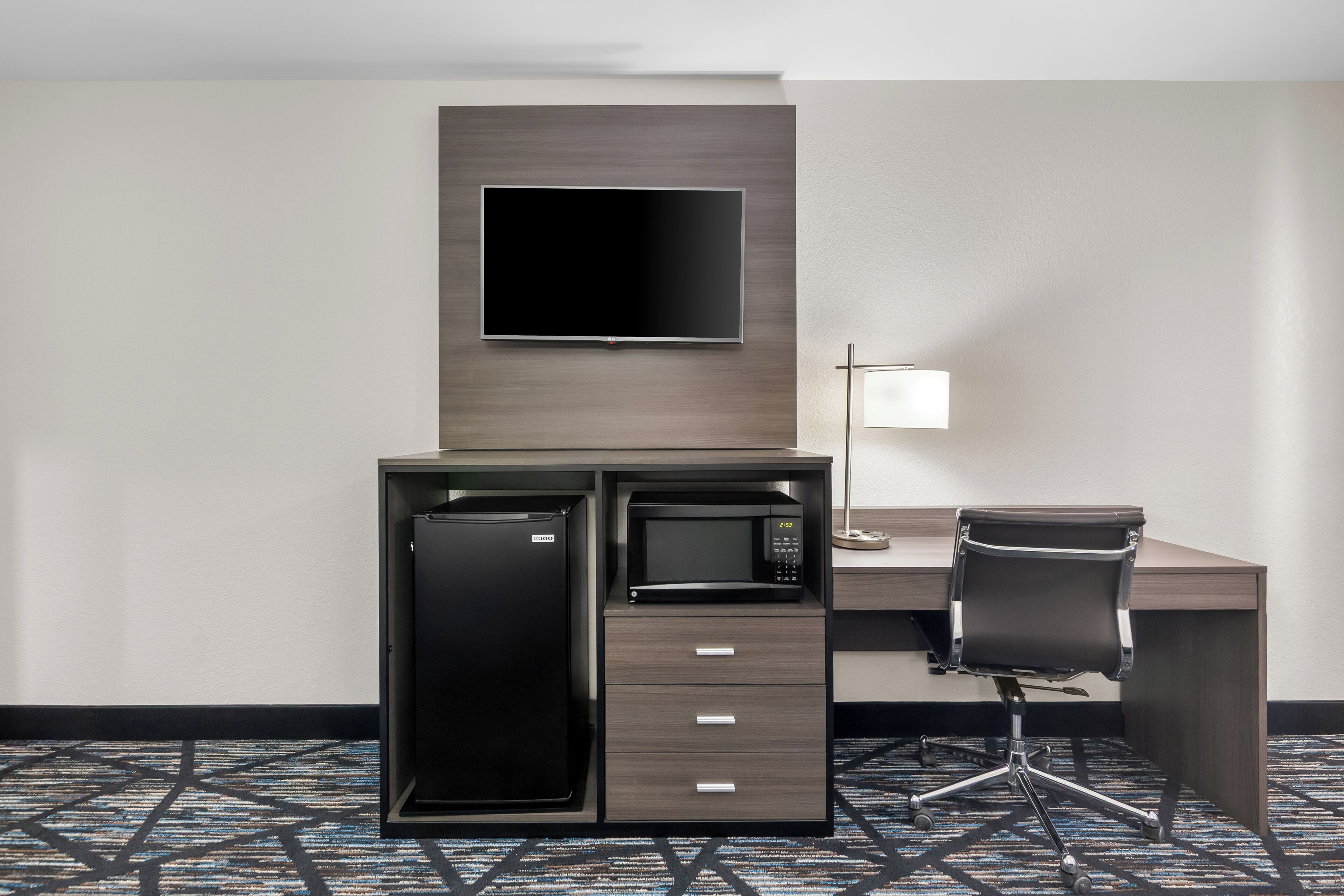 Hotelkamer met bureau, flatscreen televisie, magnetron, koelkast, stoel en lamp.