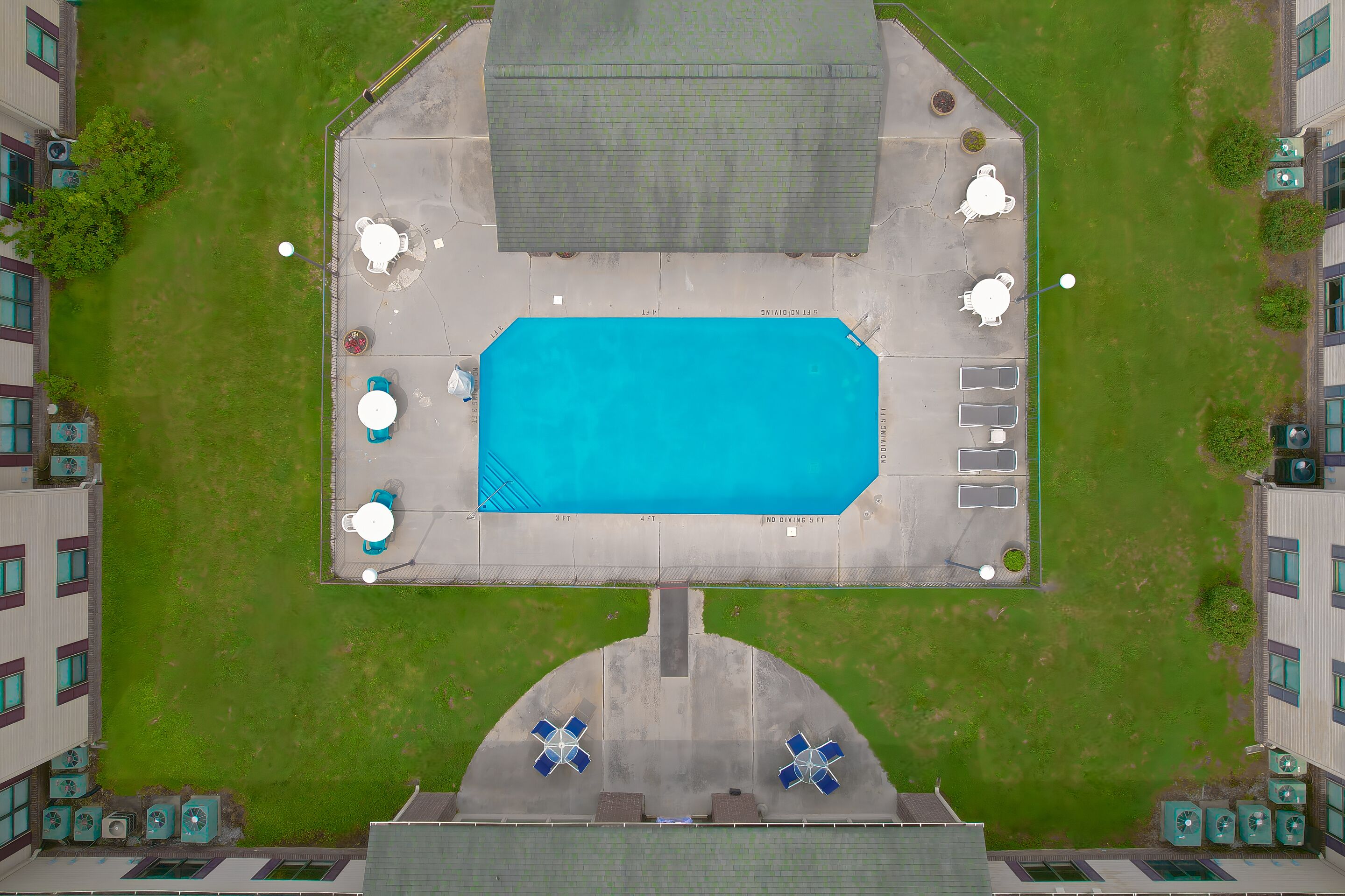 An aerial view of a swimming pool area with surrounding buildings, a covered seating area, and a parking lot.
