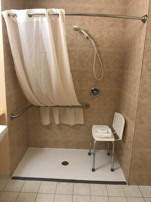 A shower area with a white shower chair and a beige shower curtain. - Best Western Plus Brunswick Bath (Brunswick)
