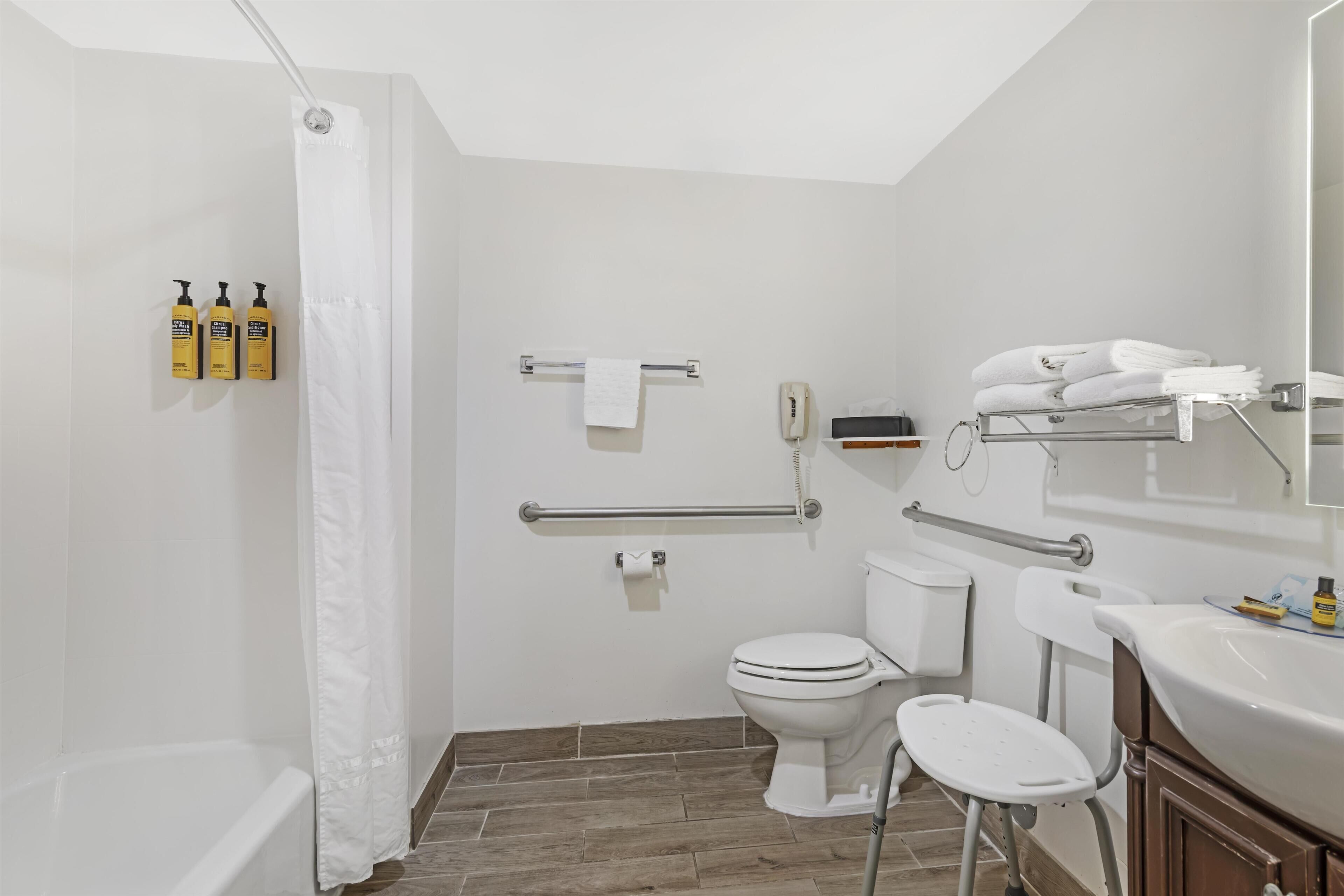 A modern bathroom with a shower, toilet, and sink, equipped with grab bars and a hand dryer.