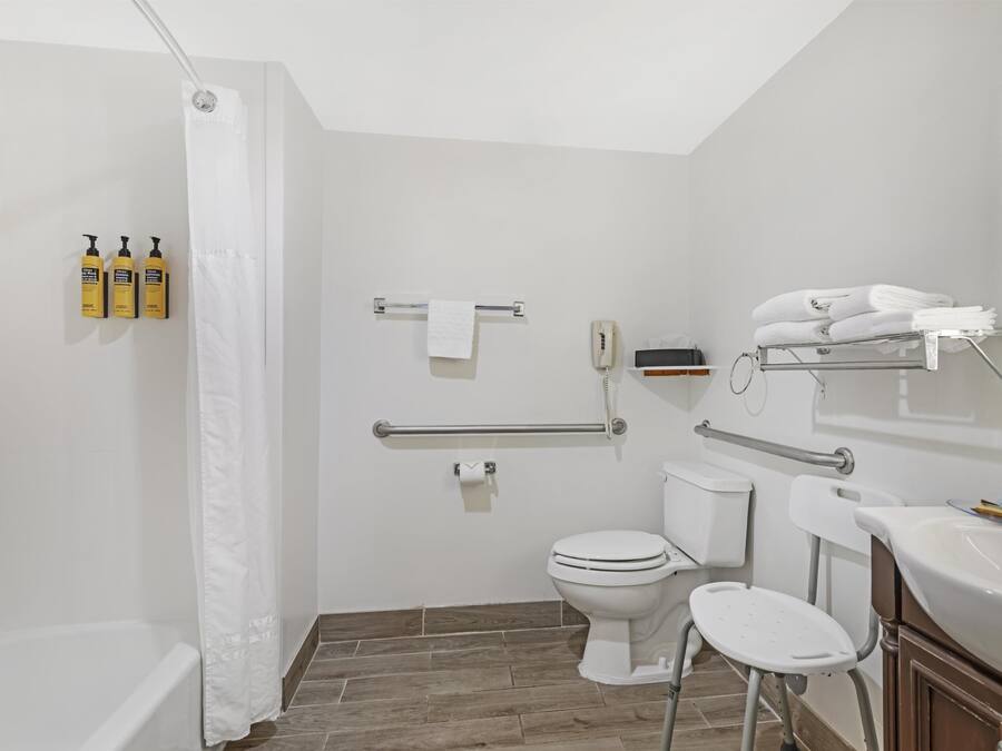 A modern bathroom with a shower, toilet, and sink, equipped with grab bars and a hand dryer.