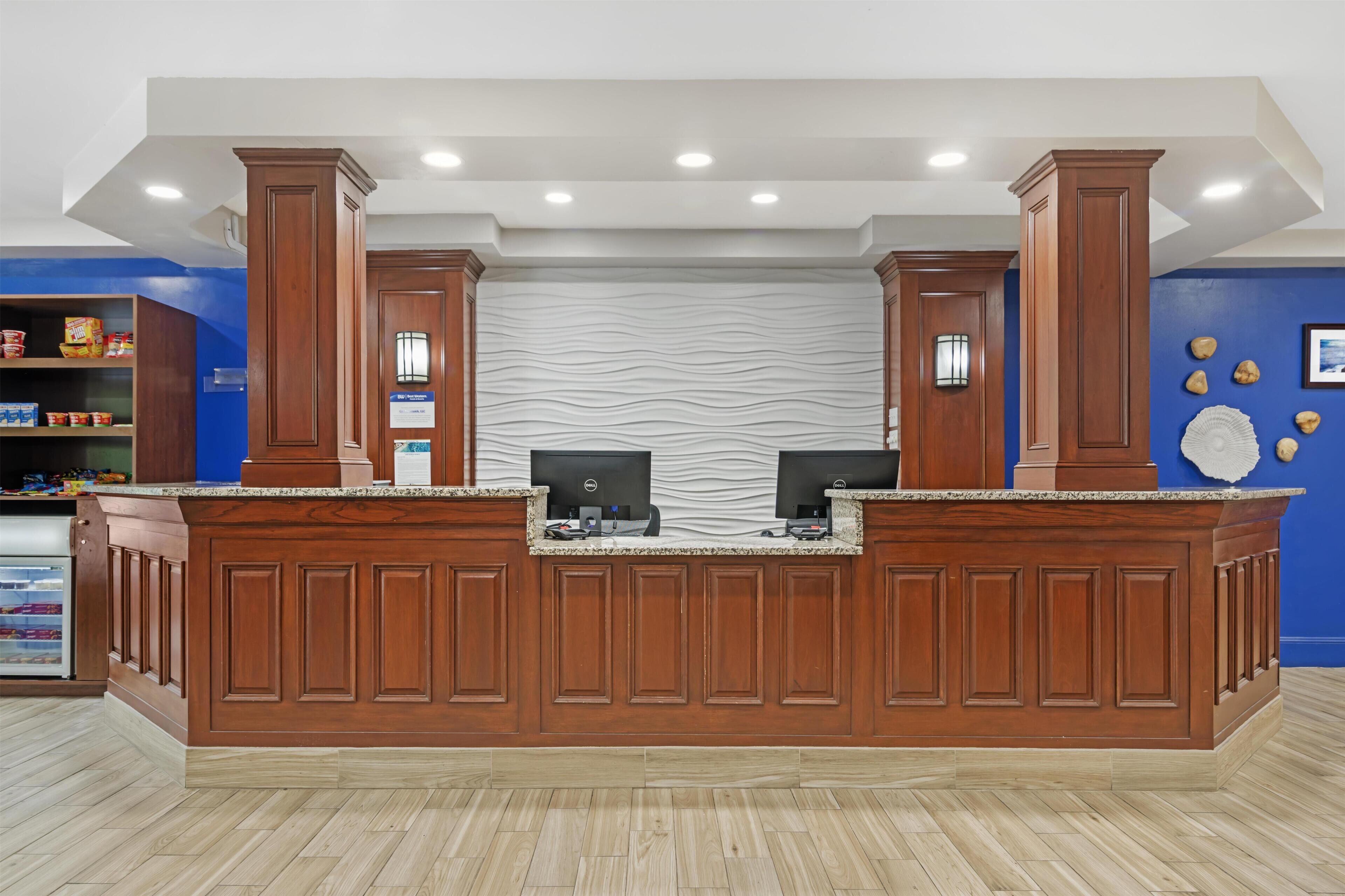 A reception desk with two computer monitors, wooden paneling, and a blue wall with decorative items.