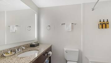 A modern bathroom with a granite countertop sink, a toilet, and a shower.