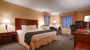 A hotel room with a large bed, two bedside tables, a desk, a chair, a desk lamp, a telephone, a microwave, and a small refrigerator.