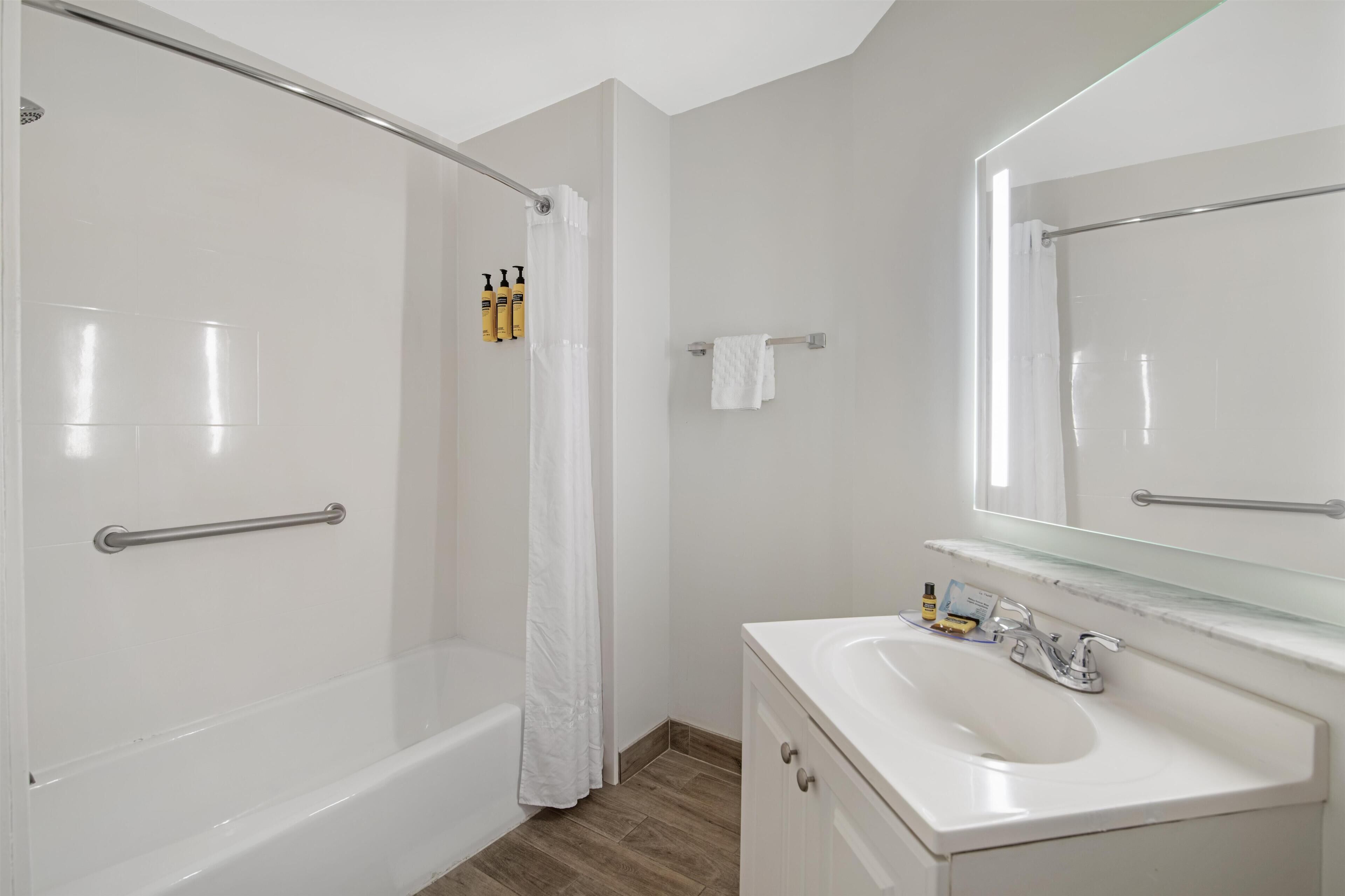 A bathroom with a bathtub, shower, vanity with a mirror, and toiletries.