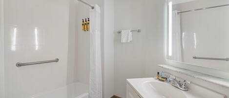A bathroom with a bathtub, shower, vanity with a mirror, and toiletries.