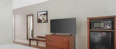 Quarto com cama, penteadeira, televisão, micro-ondas e porta.