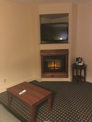 A living room with a fireplace, a television mounted above it, and a small table with a remote control. - Best Western Plus Brunswick Bath (Brunswick)