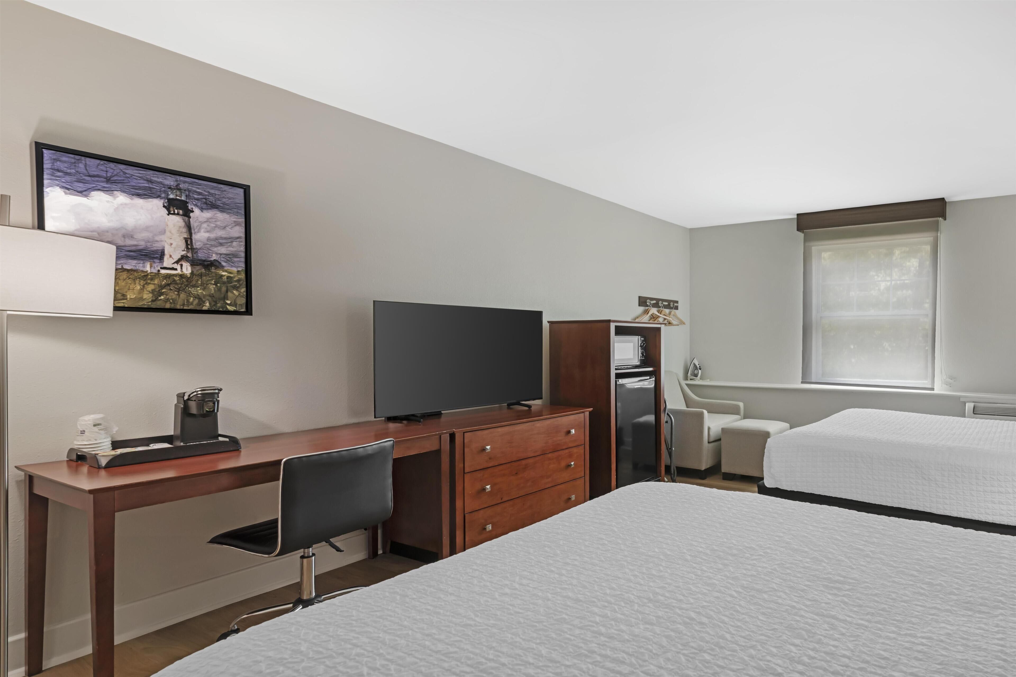 A hotel room with a bed, a desk with a chair, a television, a coffee maker, and a painting on the wall.
