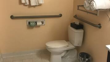 A bathroom with a toilet, handrails, a towel rack, and a trash bin.