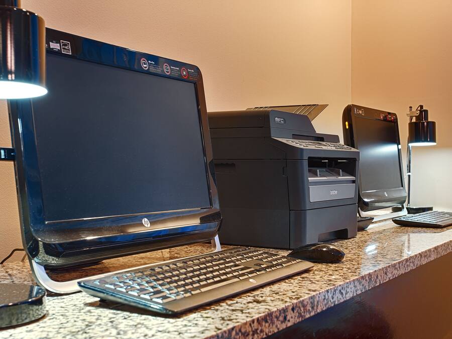 A home office setup with a desktop computer, printer, keyboard, mouse, and desk lamp.
