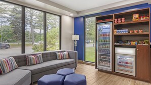 A modern hotel room with a sofa, ottomans, a refrigerator stocked with snacks, and a view of the street. - Best Western Plus Brunswick Bath (Brunswick)