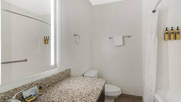 A bathroom with a granite countertop, a white toilet, a shower with a white curtain, and a mirror.