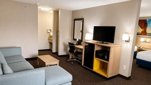 A hotel room with a sofa, a desk with a flat-screen TV, a mirror, and a bed. - Days Inn by Wyndham Rio Rancho (Rio Rancho)