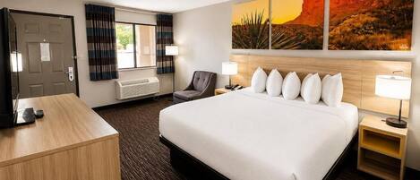A hotel room with a large bed, a desk, a chair, a TV, and a painting of a desert landscape.