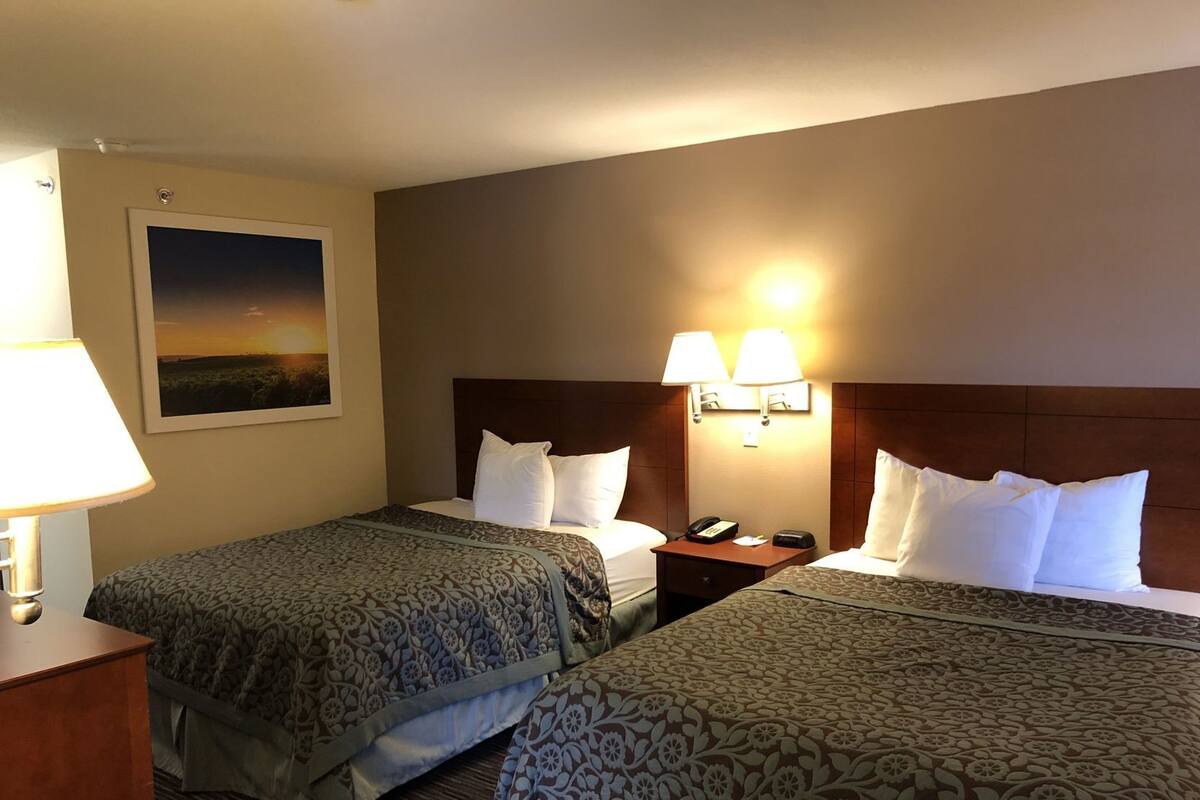 A hotel room with two beds, a nightstand, a lamp, a painting, and a wall-mounted light fixture.