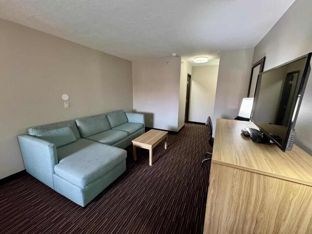 A hotel room with a sofa, a small table, a desk with a computer, and a TV.