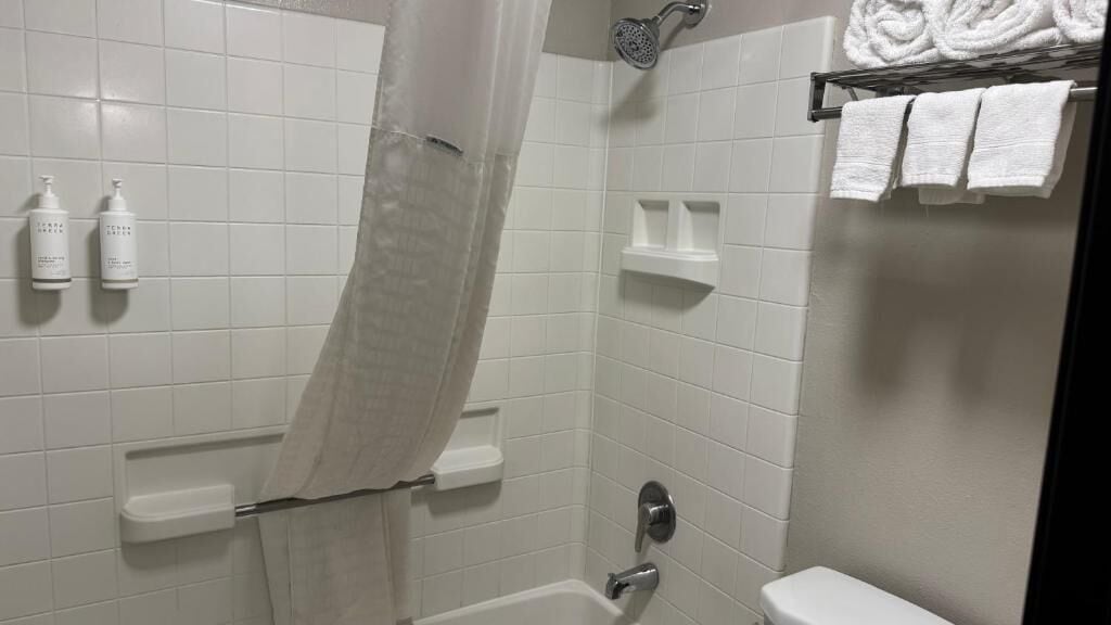 Un baño con azulejos blancos, cortina de ducha, inodoro y toallero con toallas.
