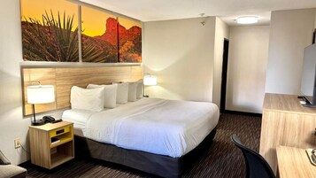 A hotel room with a bed, bedside lamps, a desk, and a television.