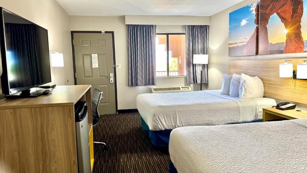 A hotel room with two beds, a TV, a desk, and a window with curtains.