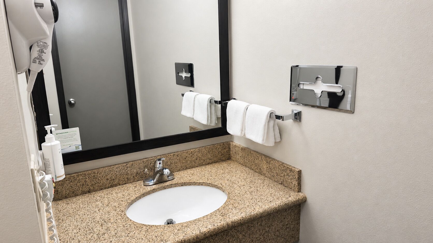 A bathroom with a granite countertop sink, a mirror, a hair dryer, and a towel rack.