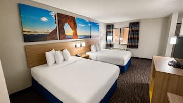 Ein Hotelzimmer mit zwei Betten, einem Schreibtisch, einem Stuhl, einem Fernseher und einem großen Fenster mit Vorhängen.