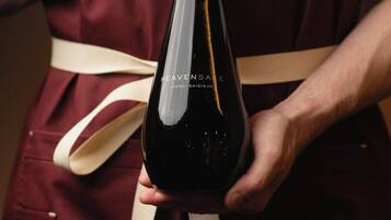 A person holding a wine bottle with a label that reads 'HEAVENSAKE JUNMAI DAIGINJO.'