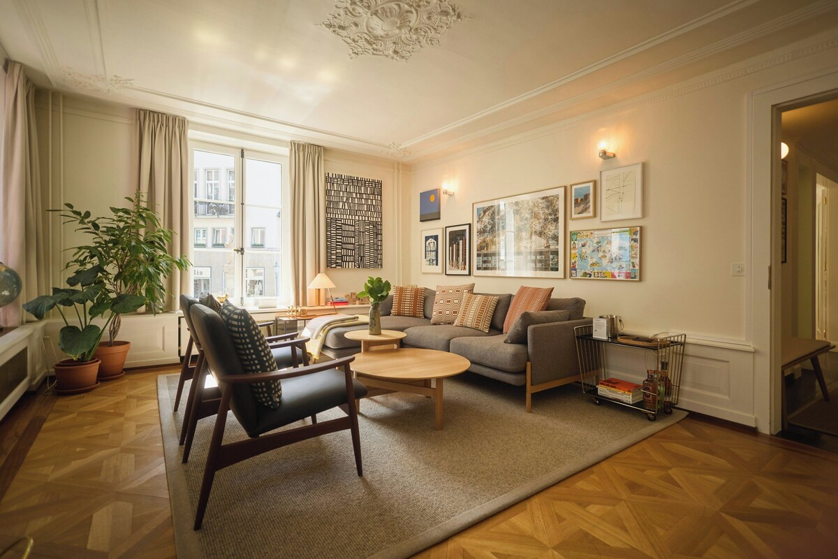 A modern living room with a sofa, armchairs, a coffee table, and a bookshelf.