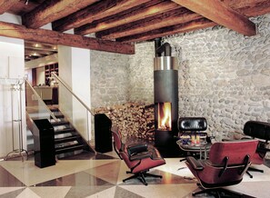 A modern interior with a stone wall, a fireplace, leather chairs, and a staircase.