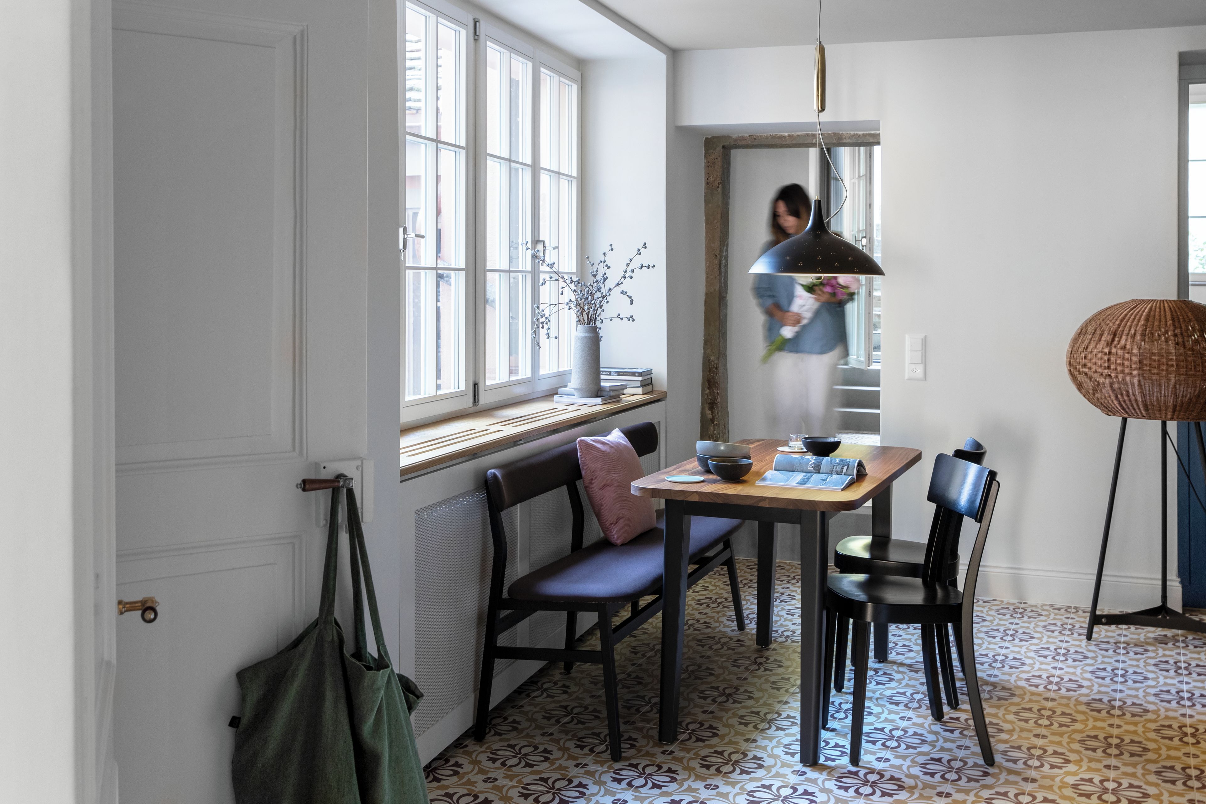 Un espace repas comprenant une table, des chaises, un banc, un vase avec des branches et une lampe suspendue.
