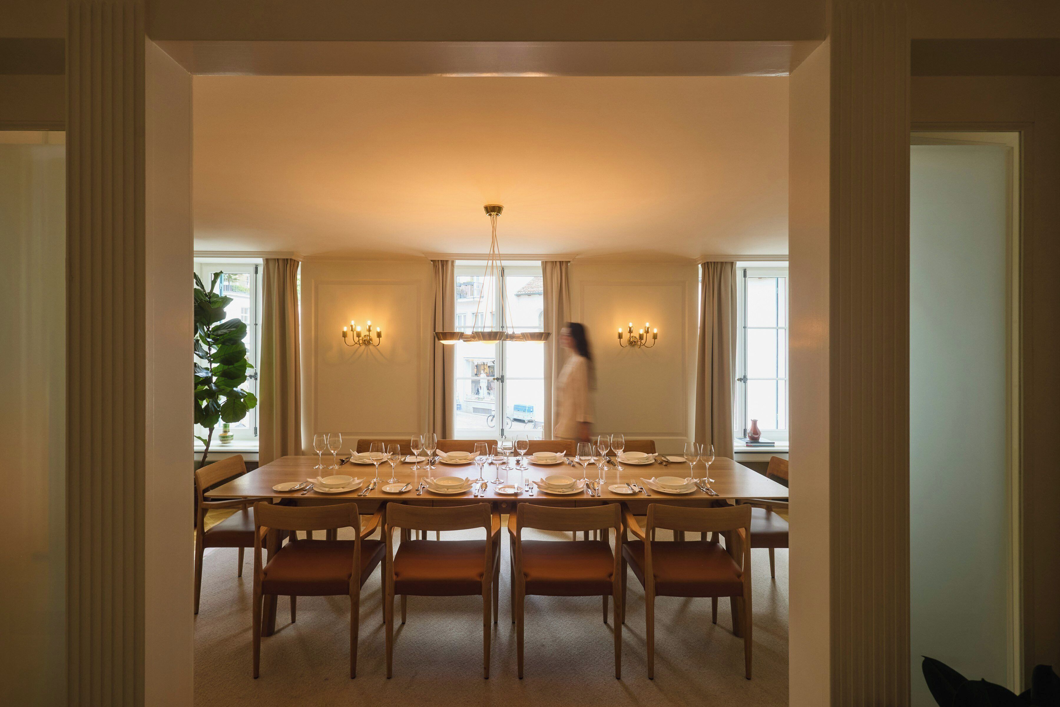 A dining room with a large table set for a meal, flanked by two wall-mounted chandeliers.
