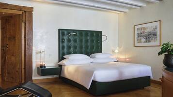 A neatly arranged bedroom with a green upholstered headboard, a bed with white linens, a bedside table with a lamp, and a framed artwork on the wall.