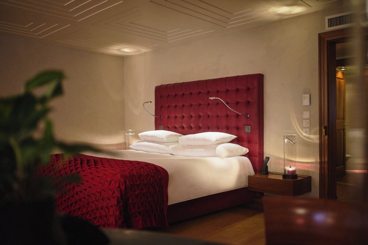 Ein ordentlich eingerichtetes Schlafzimmer mit einem geblatteten Kopfteil, einem Nachttisch mit Lampe und einer Zimmerpflanze.