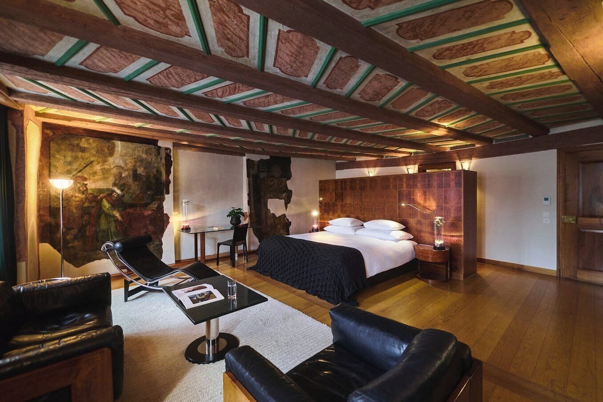 A room with a large bed, a desk with a chair, and a leather sofa.