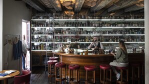 A bar with a wooden counter, multiple stools, and shelves stocked with bottles. - Widder Hotel (Zürich)