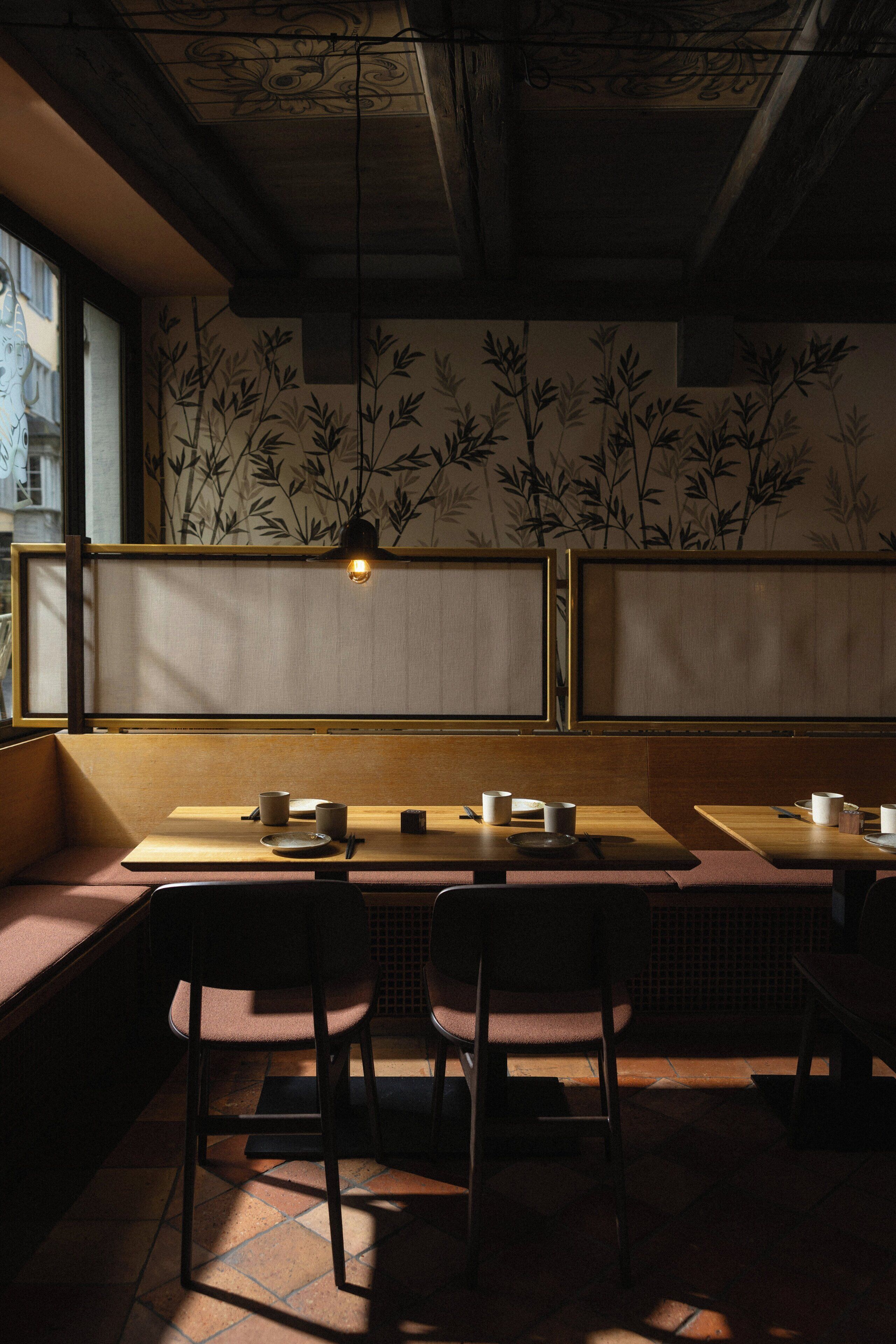 L’intérieur d’un restaurant avec des banquettes en bois, des chaises noires et un mur orné de motifs.